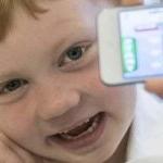 A young student in a classroom holds up a mobile phone and smiles for a photo