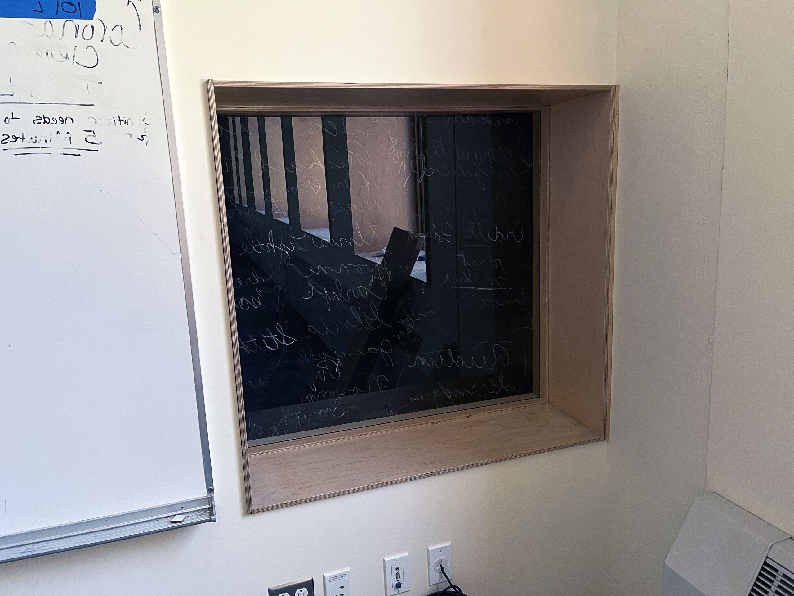 a window is inset into a wall and has a black surface with chalk writing behind the plexiglass