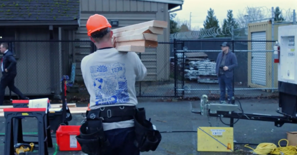 Video still from video produced by SPS students. Still shows student carrying wood and walking through construction site. 